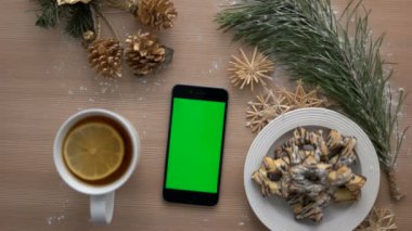 Üstten Görünüm adam akıllı telefon ile yeşil ekran kullanarak ele. Dokunarak ve dokunmatik ekran sayfalarında kaydırma parmak. Ahşap masa arka plan Christmas ayrıntılar. Chroma anahtar