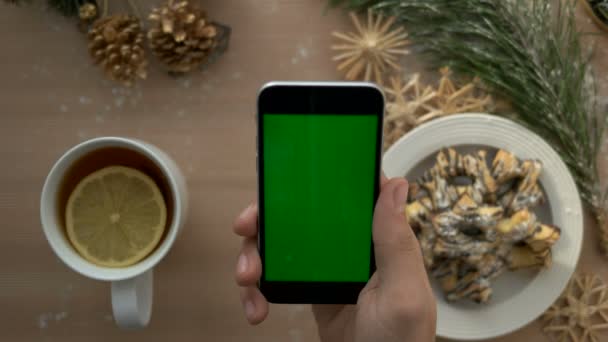 Bovenaanzicht man hand bedrijf smartphone met groen scherm. Vinger te tikken en te scrollen van pagina's op touchscreen op Kerstmis tabelachtergrond. Chromakey — Stockvideo