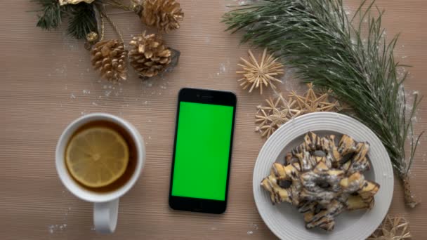 Felülnézet ember kéz használ szúró telefon-val zöld képernyő. Finger megérinti és tekerő touchscreen oldalain. Karácsonyi részletek a fából készült asztal háttere. Chroma-kulcs