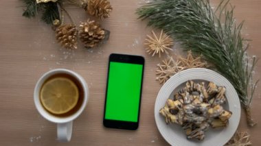 Üstten Görünüm adam akıllı telefon ile yeşil ekran kullanarak ele. Parmak dokunmatik ekran dokunarak. Noel dekorasyonları ahşap masa arka plan üzerinde. Chroma anahtar