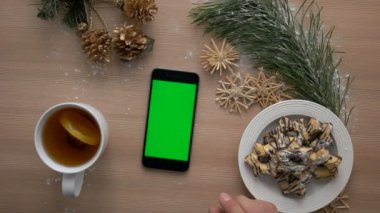 Noel dekorasyonu ile ahşap masa üzerinde yeşil ekranlı akıllı telefon kullanan adam. Rahat Noel. Üstten Görünüm. Chroma anahtar