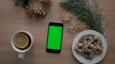 Üstten Görünüm adam akıllı telefon ile yeşil ekran kullanarak ele. Dokunarak ve dokunmatik ekran sayfalarında kaydırma parmak. Noel dekor ahşap masa arka plan üzerinde. Chroma anahtar