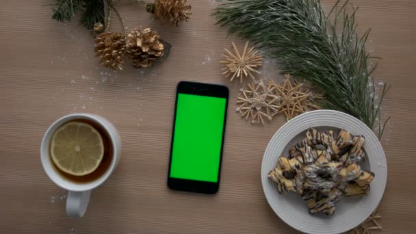 Bovenaanzicht man hand met behulp van slimme telefoon met groen scherm. Vinger te tikken en te scrollen van pagina's op touchscreen. Kerst decor op houten tafel achtergrond. Chromakey — Stockvideo