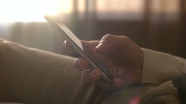 Akıllı telefon tutarak erkek ellerini kapatın. N kanepe evde otururken cep telefonu kullanan adam. Dokunmatik ekranda dokunarak