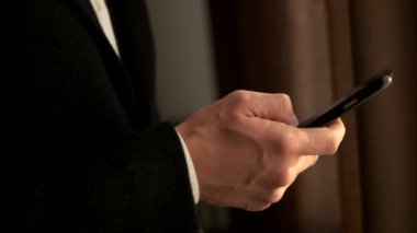 Akıllı telefon tutarak işadamı kadar kapatın. Adam el cep telefonuyla dururken pencere. Tarama, internet'te sörf dokunmatik ekran, dokunarak
