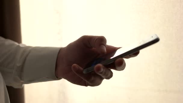 Main masculine tenant un téléphone intelligent. Homme utilisant un téléphone portable tout en se tenant près de la fenêtre. Appuyez sur l'écran tactile, surfer sur Internet. gros plan 