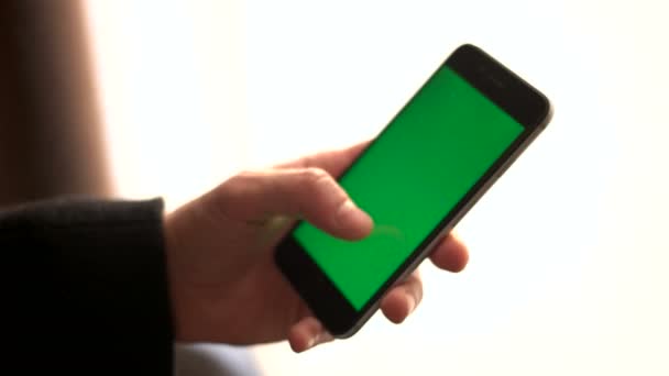 Tangan pria memegang ponsel pintar dengan layar hijau. Seorang pria menggunakan ponsel saat berdiri di dekat jendela. Tapping on touchscreen, surfing internet. tutup — Stok Video