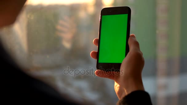 Muž, který držel chytrý telefon s zeleným plátnem. Muž, pomocí mobilního telefonu stoje u okna. Zadní pohled na výstřel. Chroma klíč — Stock video