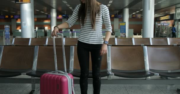 Beautiful young tourist girl with backpack and carry on luggage in international airport, waiting for her flight, looking upset. — Stock Video