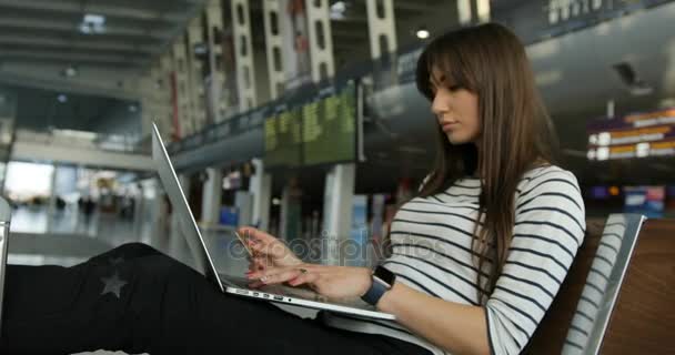 Красивая молодая пассажирка совершает онлайн-покупки с помощью кредитной карты на ноутбуке в ожидании в международном аэропорту — стоковое видео