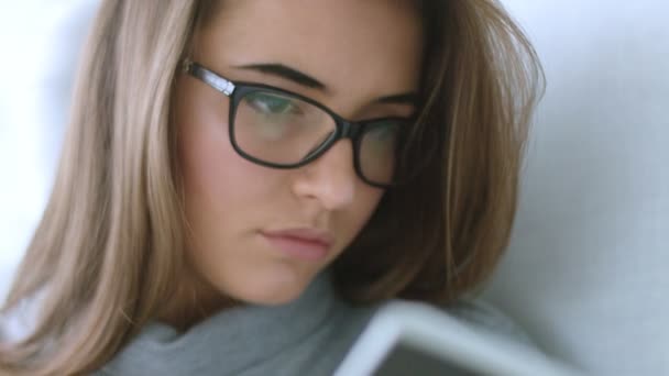 Vista de cerca de la atractiva joven morena en gafas relajándose en casa en el sillón leyendo un libro — Vídeo de stock