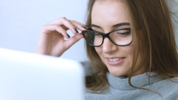 Привлекательная девушка в очках улыбается во время использования ноутбука — стоковое видео