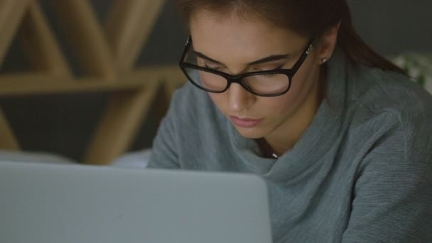 Молодая женщина в очках смотрит на монитор, просматривает интернет — стоковое видео