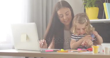 Ev zemin üzerine hamuru ile onun dauther açılış kutusunu dizüstü bilgisayarda yazarak siyah uzun saçlı güzel beyaz kadın.