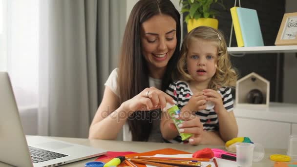 Мама с дочерью делают пузырьковый воздуходув. Молодая красивая женщина и маленькая девочка с кудрявыми светлыми волосами сидят на столе в комнате . — стоковое видео