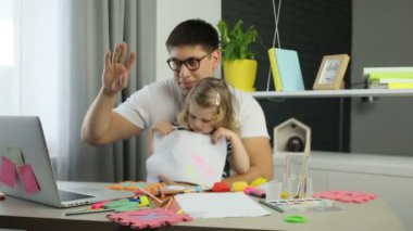 Yakışıklı adam gözlük ve ev ve video annesiyle sohbet içinde masanın üstüne sarı kıvırcık saçlı siting ile onun küçük dauther. Kapalı.