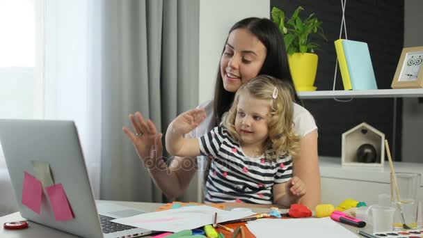 Jovem mulher com cabelos longos pretos e sua filha com cabelo encaracolado loiro vídeo conversando com o pai no laptop em casa fundo . — Vídeo de Stock