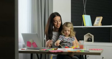 Uzun siyah saçları ve onun dauther boyalar üzerinde ev arka plan kullanarak sarı kıvırcık saçlı çizim ile olan genç ve güzel kadın. Kapalı.