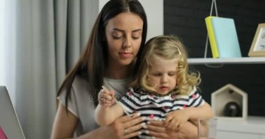 Sarışın kıvırcık saçlı sevimli küçük beyaz kız ve annesi uzun siyah saçlı kullanarak çizim evde siting boyar. Kapalı.