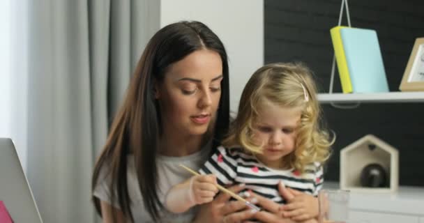 Piccola ragazza caucasica con un disegno biondo riccio. Giovane donna in cerca di camer siting con il suo papà in casa. Interni . — Video Stock