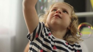 Charmind portresi sarı kıvırcık saçlı ve mavi gözlü kabarcık üfleyici ile ev arka planda çalmaya ile beyaz küçük kız. Kapalı.