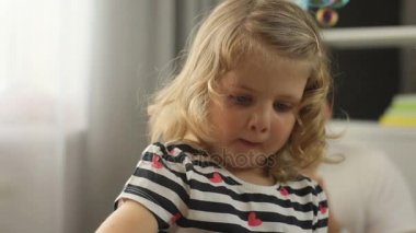 Sarı kıvırcık saçlı ve mavi gözlü ev kabarcık üfleyici ile oynarken oldukça küçük kız portresi. Kapalı.