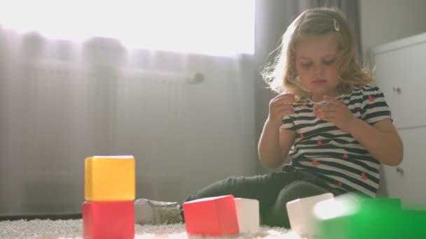 Kaukasische schöne kleine Mädchen mit blonden lockigen Haaren spielen mit kleinen Spielzeug Sitzen auf dem Boden in der Heimat. Innenräume. — Stockvideo