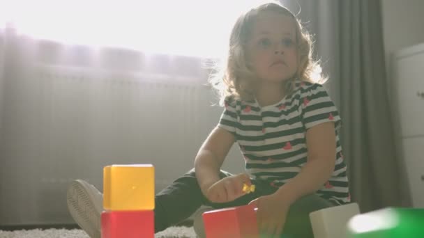 Vista lateral da menina bonita caucasiana com cabelo encaracolado loiro situado no chão em casa e brincando com pouco brinquedo. Interior . — Vídeo de Stock