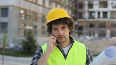 Çekici beyaz Oluşturucusu'nda sarı kask ve akıllı telefonda konuşurken ve çizim elinde tutan yeşil yelek. Açık.