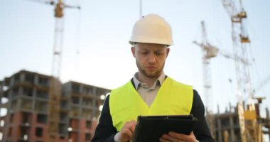 Genç Oluşturucusu'nda beyaz kask ve tablet için iş kullanma inşaat sahasında yeşil yelek yoğunlaşmıştır. Açık.