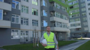 Yakışıklı Oluşturucu rousse saç ve sakal beyaz kask elinde tutan ve kamera için arka plan üzerinde gidiş ile ev inşa etti..