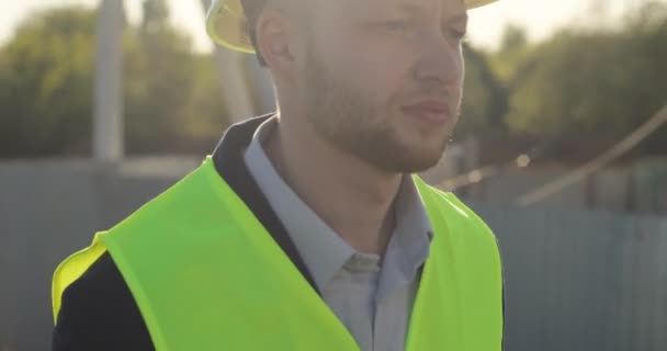 Portret van ernstige Kaukasische bouwer in een groen vest gaan in aanvankelijke stadium van de bouw. Buiten. — Stockvideo