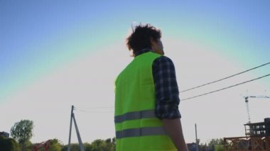 Arkadan görünüşü yeşil yelek inşaat süreci üzerinde seyir siyah kıvırcık saçlı kafasında kask bitmemiş inşaat zemin üzerine koyarak Oluşturucu.