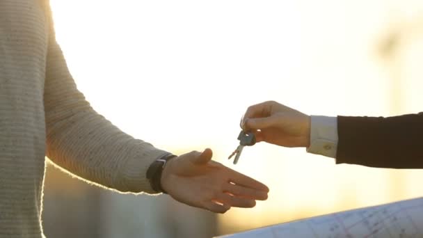 Porträt der Hand des Architekten, der dem Kunden Schlüsselanhänger gibt. zwei Männer beim Händeschütteln vor Sonnenuntergang. Außenbereich. — Stockvideo