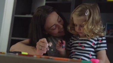 Sarı kıvırcık saçlı ve uzun siyah saçları çizim kalem ve keçeli kalem kağıt üzerine annesiyle güzel küçük kız. Kapalı.