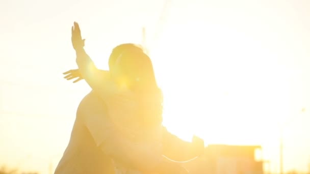 Jeune couple souriant sur fond de coucher de soleil. Jeune homme embrassant et levant les mains de la jeune femme et souriant. Extérieur . — Video