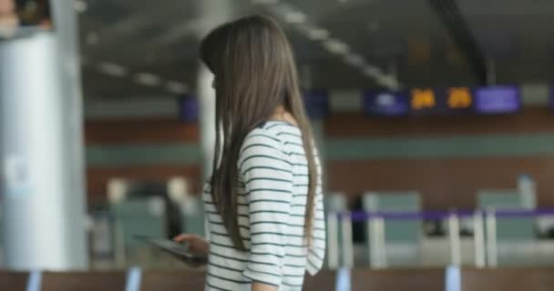 Attraktiv ung kvinna med surfplatta kommer till zonen lounge och sitta på bänken i internationella flygplats. — Stockvideo
