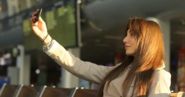 Selfie akıllı telefonda alarak ve havaalanında fotoğraf makinesinde poz çekici kadın. Yan görünüm.