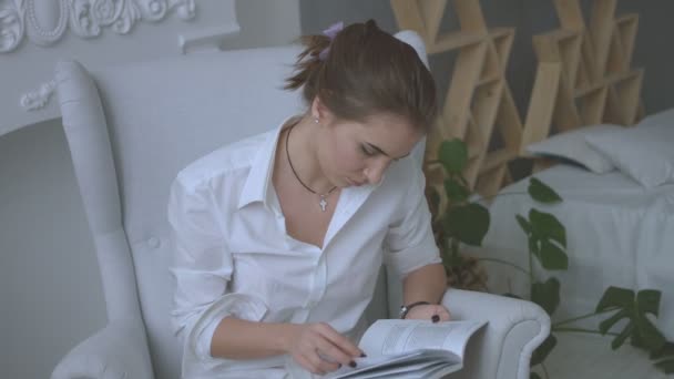 Poryrait of young woman in white casual clothes getting ready to exams while sitting in chair in the living room. Close up. — Stock Video