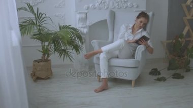 Genç çekici kadın evde kötü Oda sandalyede oturan ve tablet kullanma.