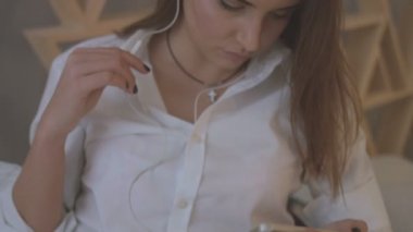 Genç kadın rahat gömlek evde yatakta yatarken kulaklık müzik dinleme.