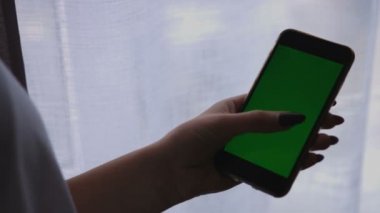 Akıllı telefon ile yeşil perde pencere arka planda tutan eller kadın. Chroma anahtar
