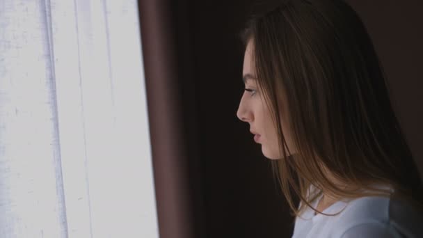 Крупним планом портрет молодої жінки, що стоїть біля вікна, повернутися до камери і посміхаючись . — стокове відео