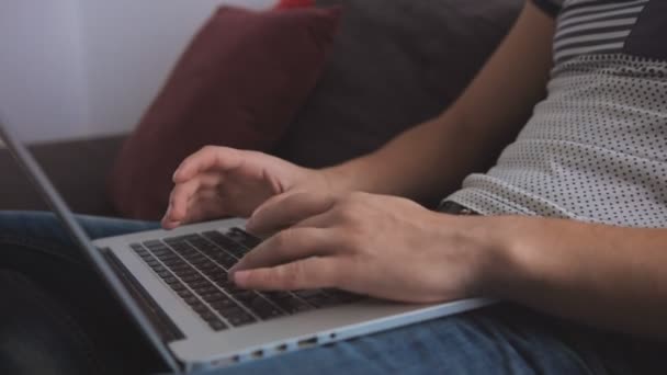 Gros plan de mains de jeunes hommes tapant quelque chose sur un ordinateur portable assis sur un canapé dans le salon . — Video