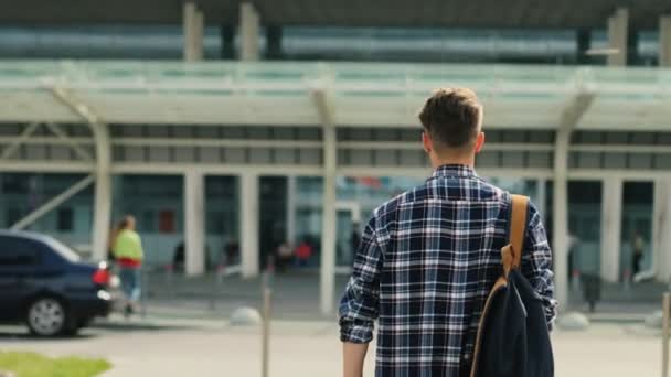 Jonge man wandelen naar de moderne luchthaven terminal voor zijn vlucht. Uitzicht vanaf de achterkant. — Stockvideo