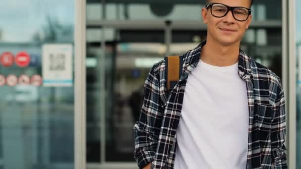 Joven hombre atractivo en las gafas caminando desde la moderna terminal del aeropuerto de su vuelo. Retrato plano . — Vídeo de stock