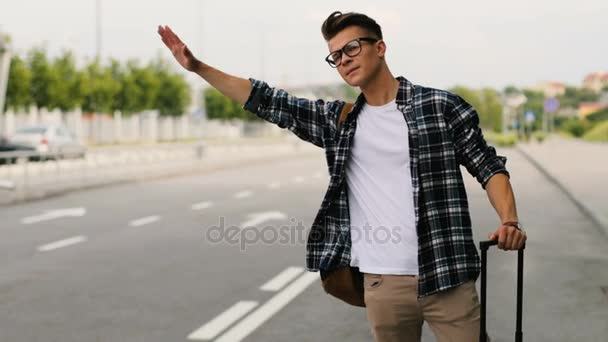Молодой человек с багажом автостопом на дороге в летний солнечный день некоторые автомобили в аэропорту . — стоковое видео