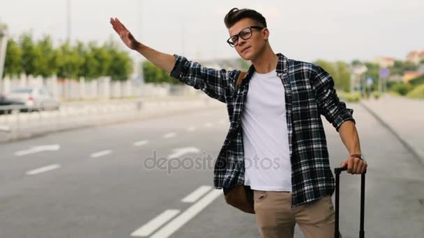 Joven con equipaje autostop en la carretera en verano día soleado algunos coches en el aeropuerto . — Vídeos de Stock