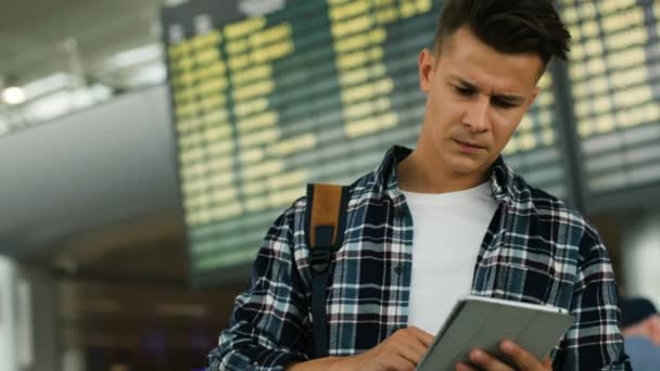 Attractive serious man in casual shirt using tablet for chatting with friends on the arrivals table background. Close up shot. — Stock Video