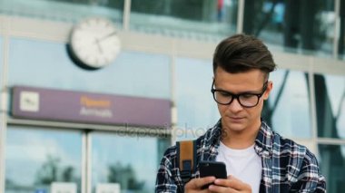 Modern Havaalanı arka plan üzerinde ağ sohbet için akıllı telefon kullanarak gözlüklü genç şık adam. Yakın çekim.